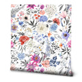 Floral wallpaper with multicolor blooms in pink, blue, purple, orange, and white, accented by black and gray leaves on a white background, in a botanical illustration style.