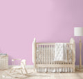 Pink wallpaper with repeating white circular motifs shown in a nursery setting with light wood furniture and neutral textiles.