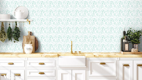 White and teal scroll-patterned wallpaper displayed in a kitchen with white cabinetry, brass accents, and natural wood surfaces.