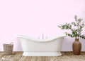 Bathroom with light pink wallpaper featuring a small flamingo pattern, white freestanding bathtub, wicker basket, and potted plant on wooden flooring.