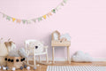 Soft pink ornamental wallpaper displayed in a children’s room with wooden furniture and playful pastel decorations.