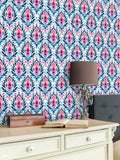 
Pink and blue floral wallpaper in a bedroom setting with cream furniture and vintage lamp decor.