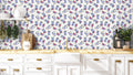 Floral wallpaper with purple, red, and cream flower bouquets shown in a bright kitchen with white cabinets and brass accents.