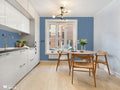 Blue geometric floral wallpaper in a contemporary kitchen with wooden dining furniture and white cabinetry.