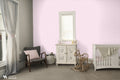 Soft pink ornamental wallpaper shown in a baby’s nursery with neutral furnishings and a cozy, classic design.