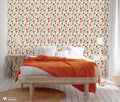 Botanical wallpaper with orange, yellow, and teal flowers and dark leaves on a cream background, shown in a cozy bedroom with white and orange accents.