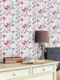 Botanical wallpaper with colorful flowers in pink, purple, blue, and orange tones on a white background, displayed in a classic interior with a cream desk and decorative lamp.