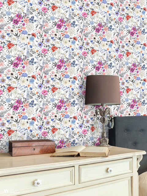 Botanical wallpaper with colorful flowers in pink, purple, blue, and orange tones on a white background, displayed in a classic interior with a cream desk and decorative lamp.